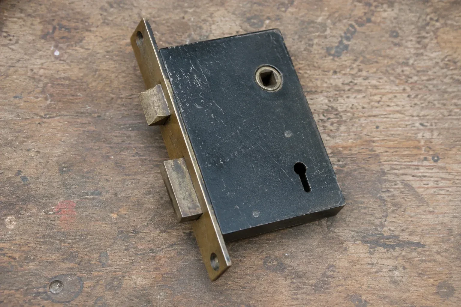 Closed mortise lock case with spindle opening, keyhole, latch and deadbolt on a wooden workbench. — Vintage Mortise Lock Service, London