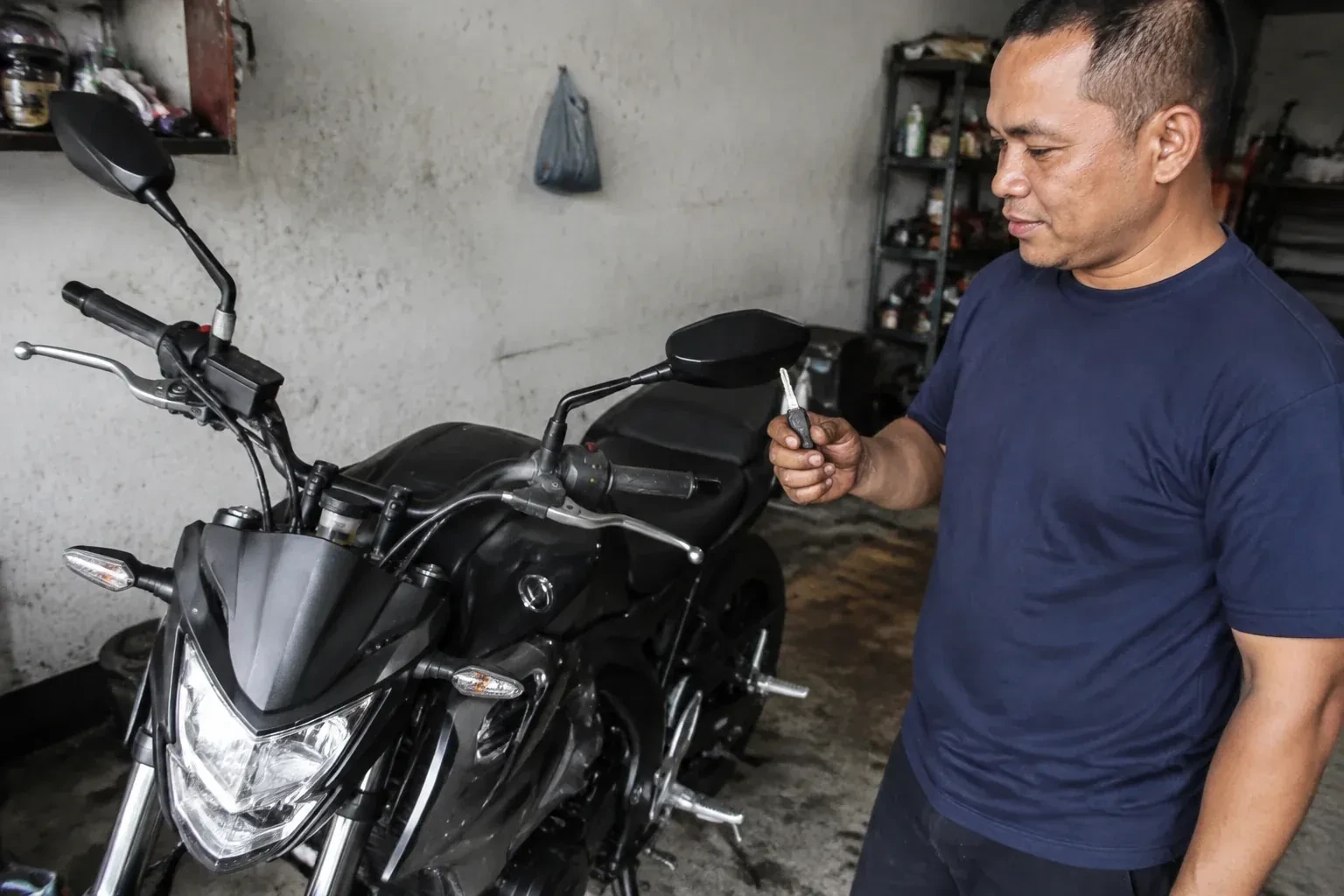 Person holding a key beside a black motorcycle in a garage. — Motorcycle & Scooter Keys, London