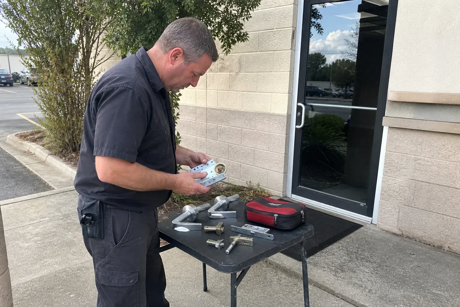 Technician examining detached commercial lock hardware on a table outside a shop entrance. — Business Lockout Service, London